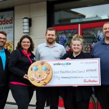 Owners of Tim Hortons stand in front of Tim Hortons holding large cheque