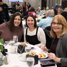 Three women sitting at table, smiling for camera