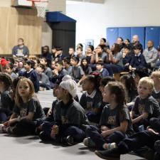 Students sitting on the floor and parents/staff sitting in chairs at assembly