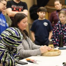 Students and staff watching a demonstration of making a drum.